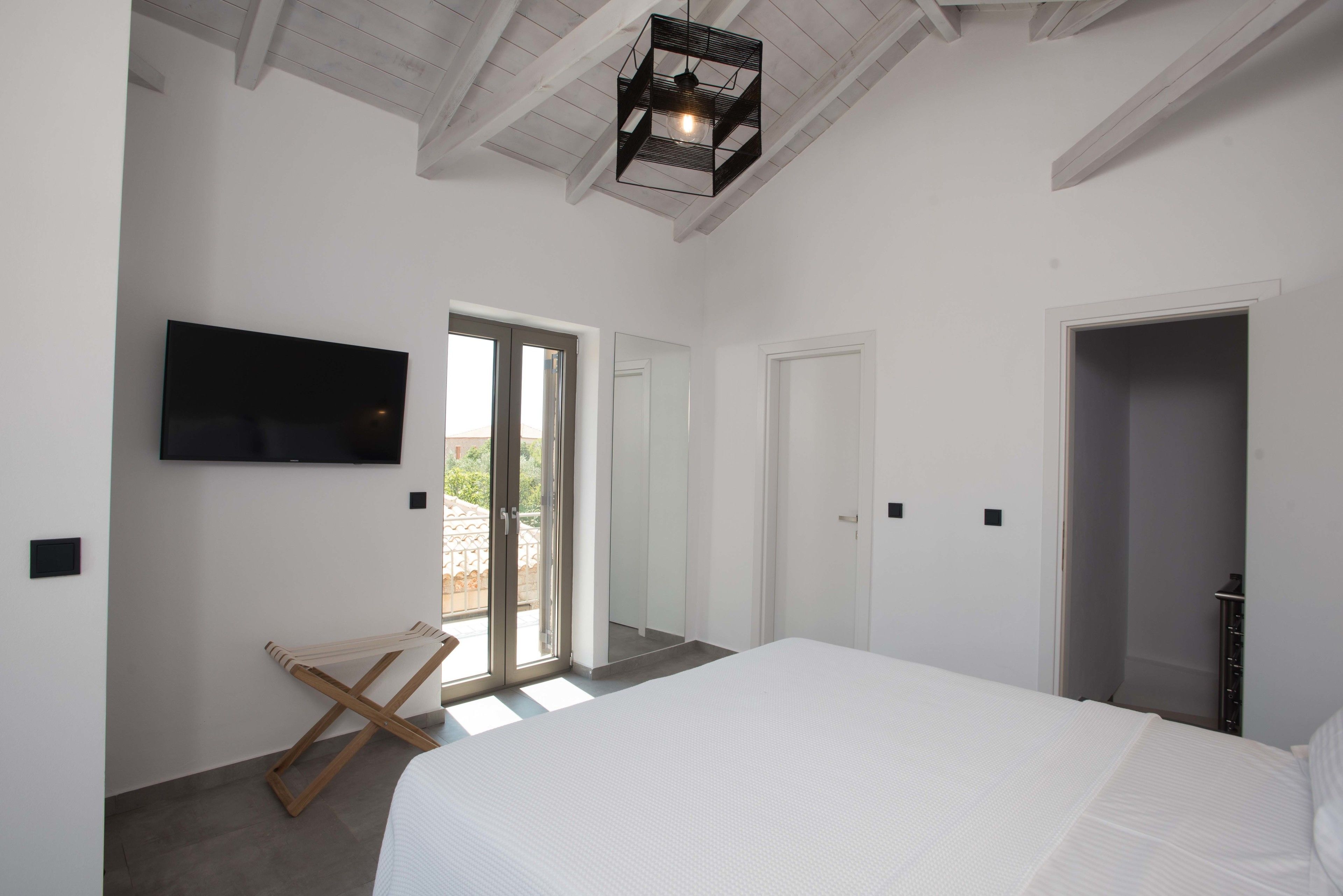 A bedroom with a large bed, a TV mounted on the wall, and a sliding glass door leading to an outdoor area.