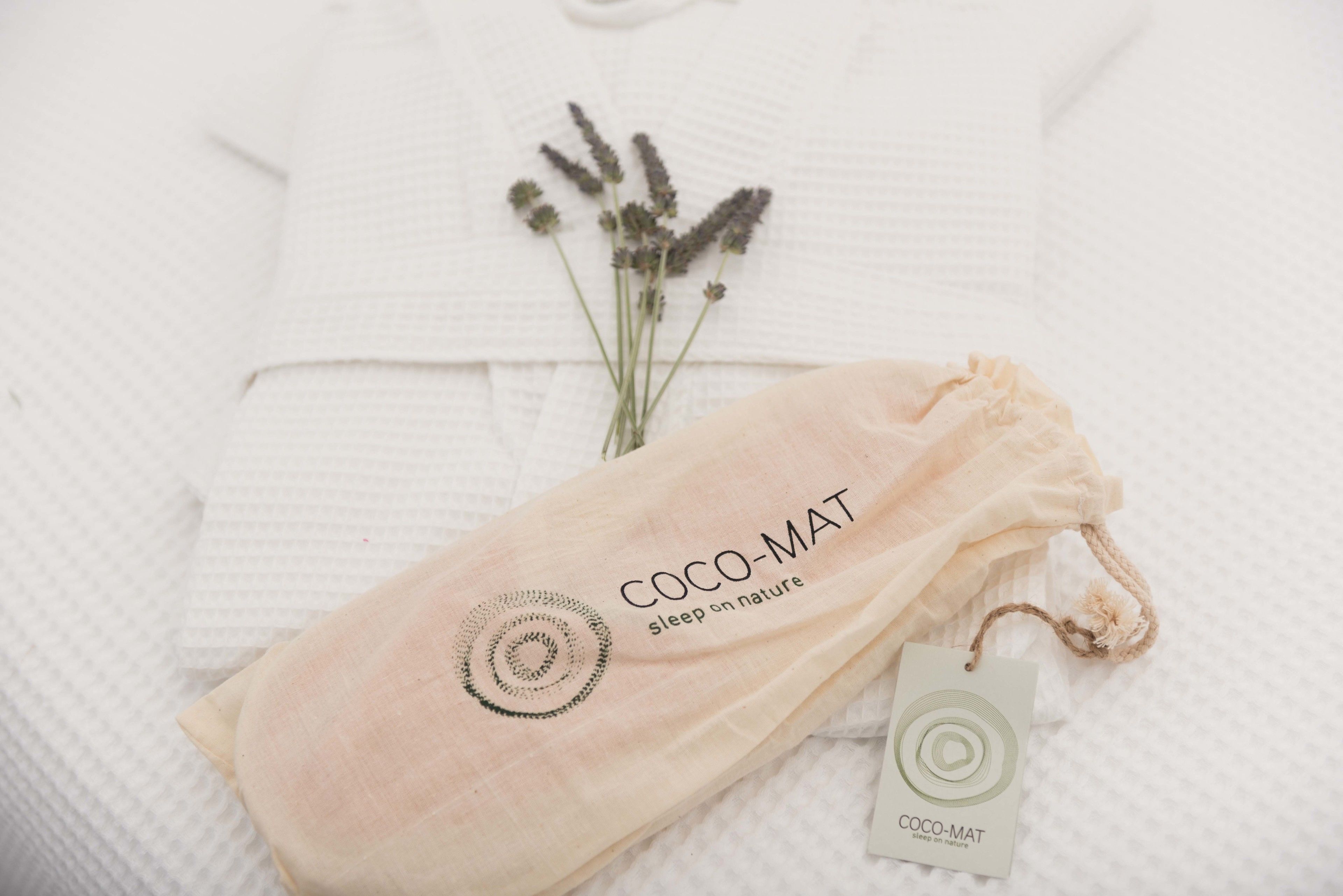 A white textured fabric with a logo and text reading "COCO-MAT sleep on nature" and a tag.