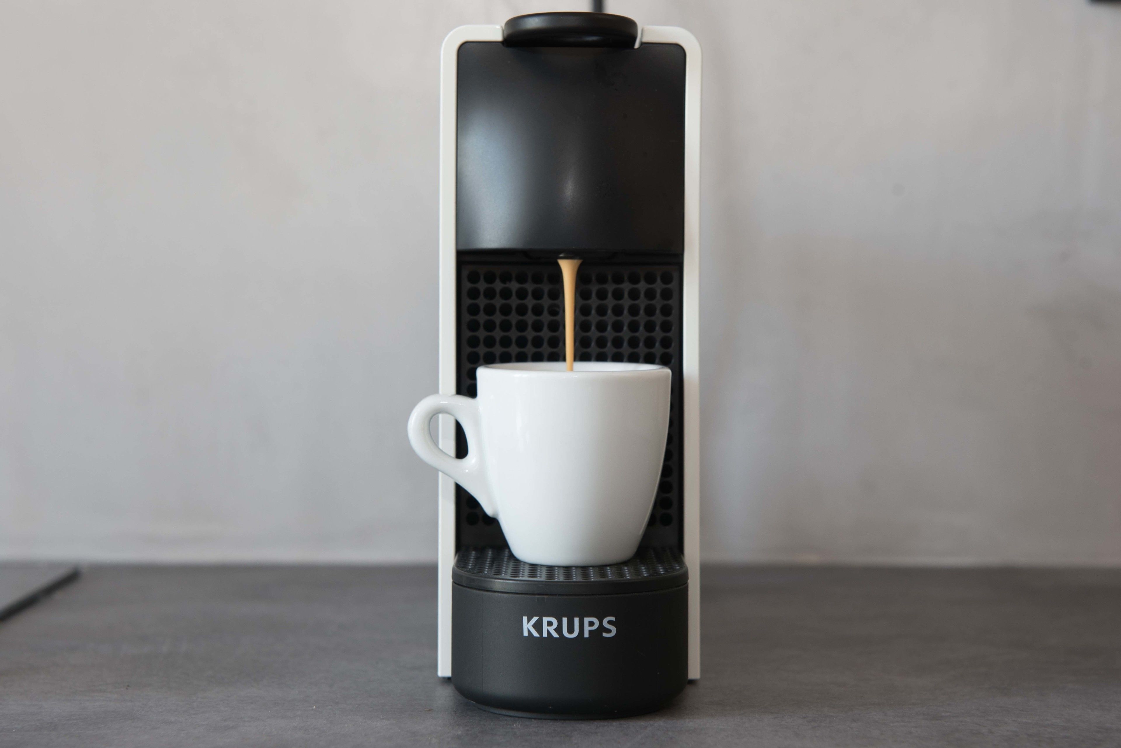 A Krups coffee machine with a white cup placed on its base.
