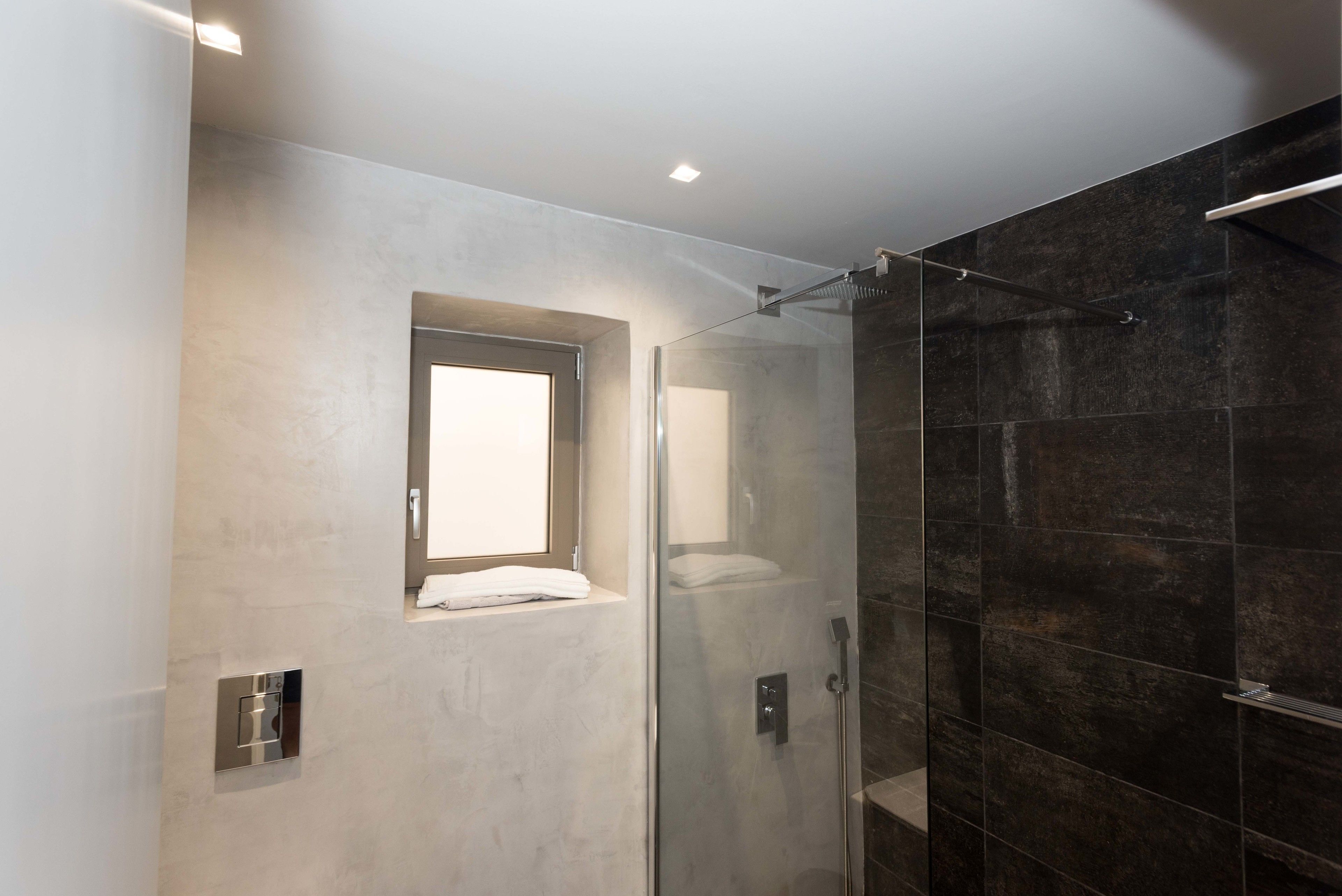 A modern bathroom with a glass shower enclosure, a built-in window, and a towel rack.