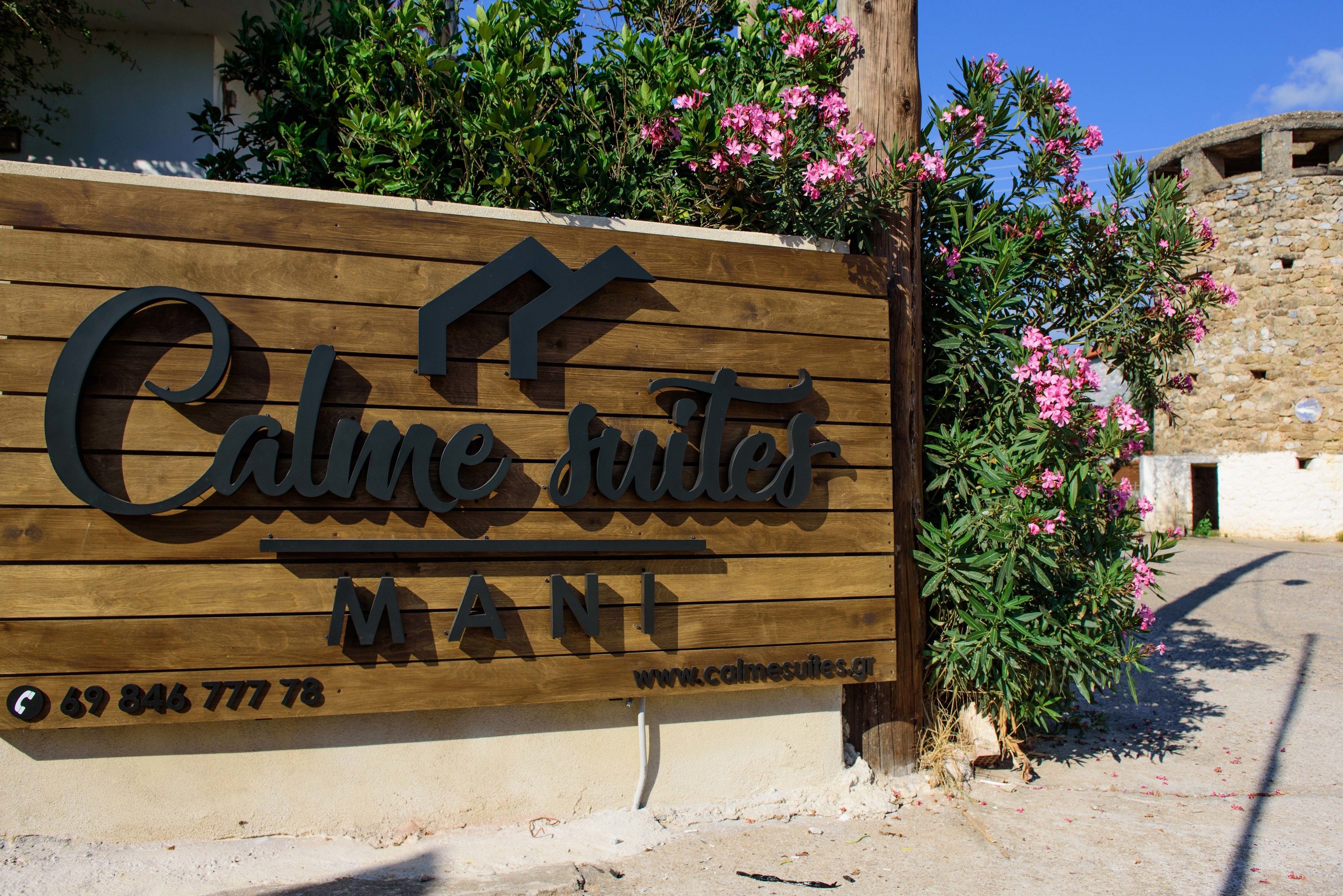 A wooden sign with the text "Calmes Suites MANI" and a website address.