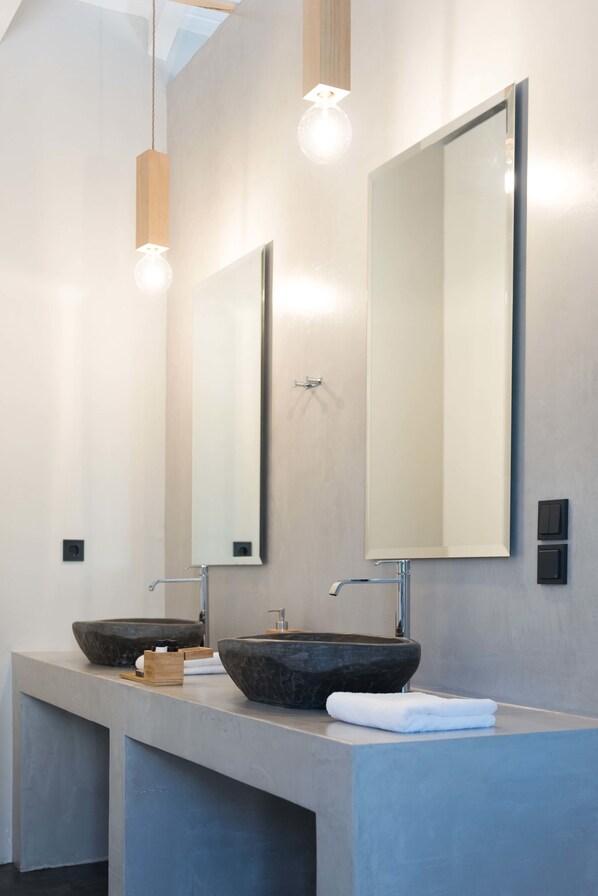 A modern bathroom with two large, dark stone sinks, a large mirror, and pendant lighting.