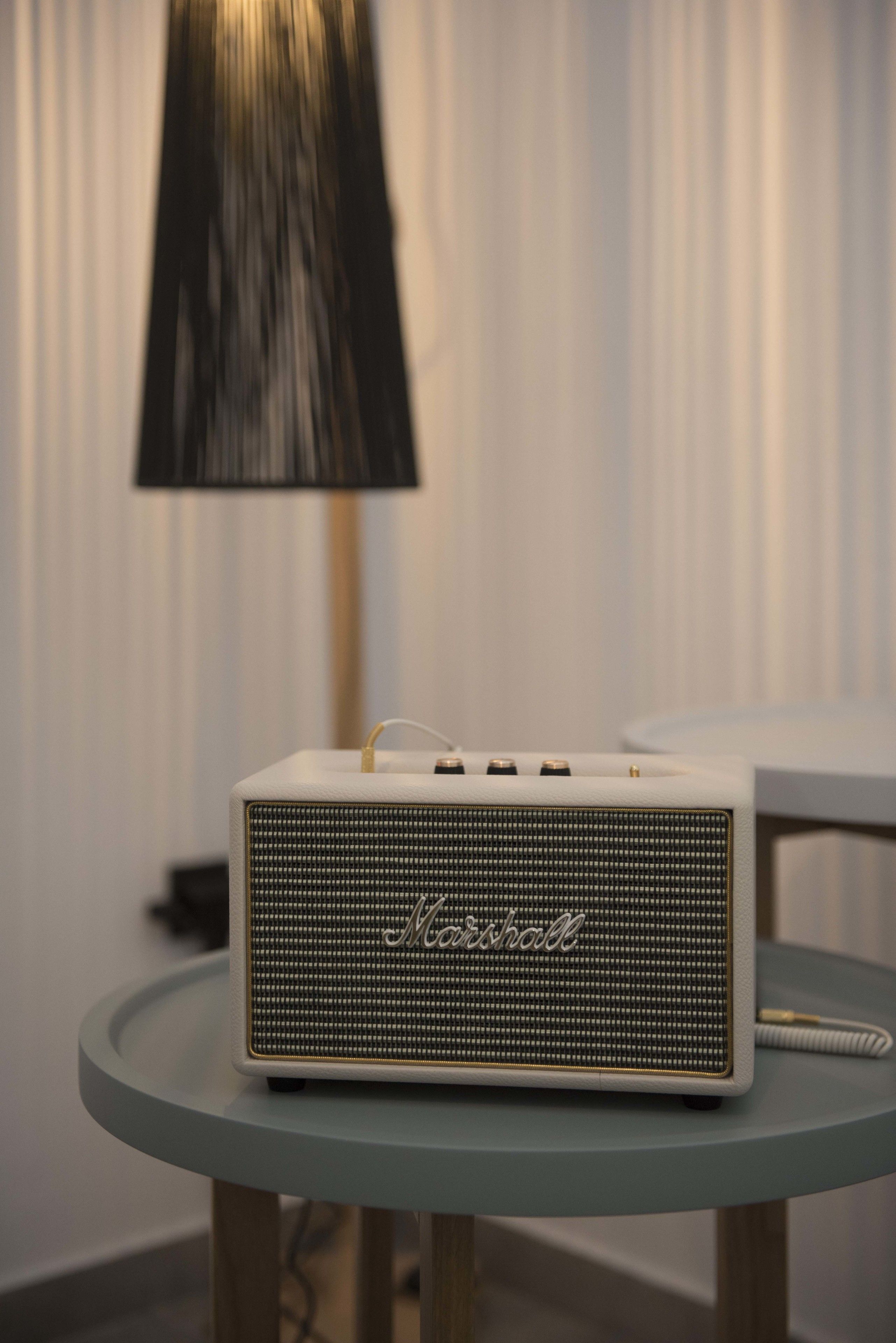 Un altavoz Marshall sobre una mesa redonda, con una lámpara al fondo.