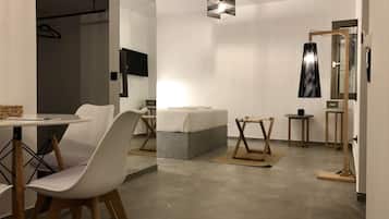 Quarto de hotel moderno com cama, mesinha, cadeira, espelho e luminária suspensa.