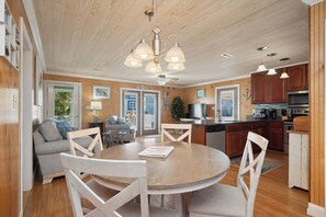 A modern kitchen with wooden cabinets, a central island, and a dining area with a round table and chairs.