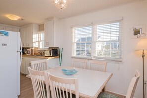 Una cocina luminosa con armarios blancos, una mesa de comedor con sillas, un microondas y una ventana con persianas.