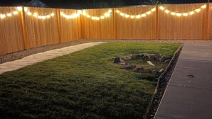 A backyard with a wooden fence, string lights, a paved walkway, and a grassy area with rocks. - Fantastic Denver Location! 5 mins from every major highway! Mountain & Lake View (Denver)