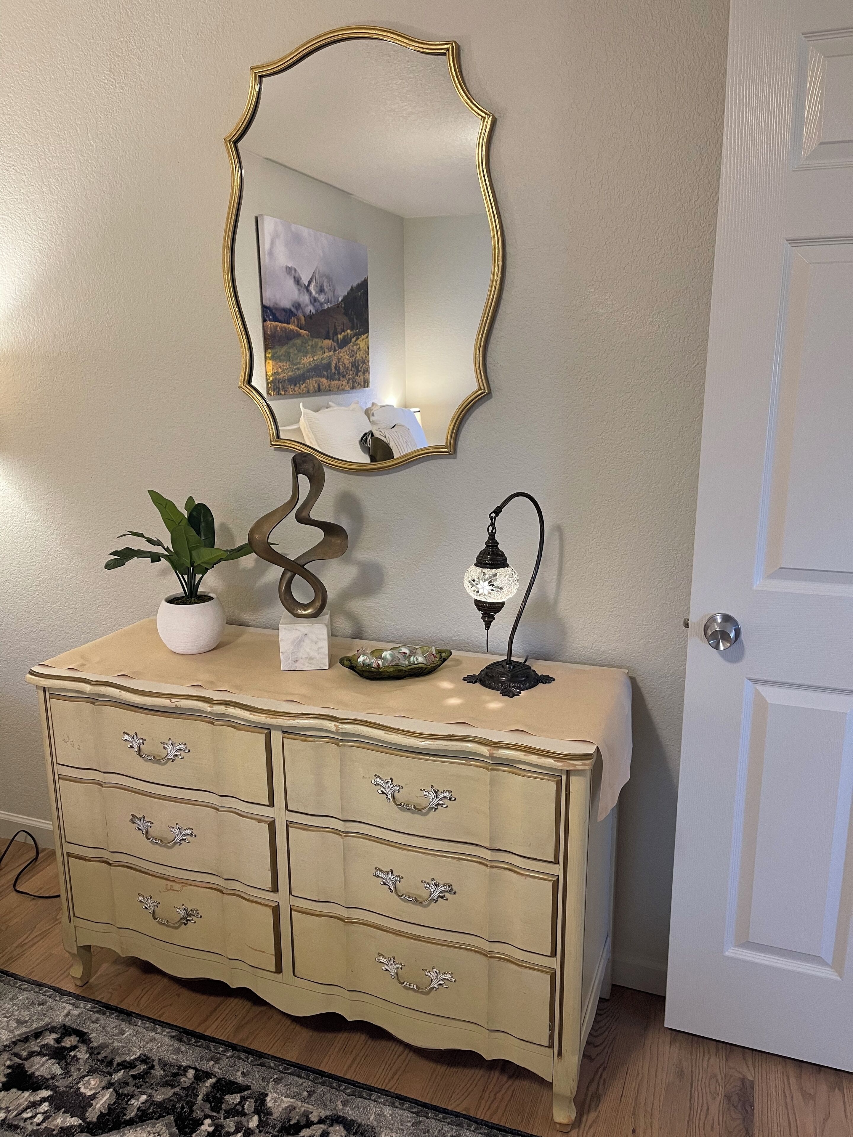 A vintage-style dresser with a mirror, a potted plant, and a decorative lamp.