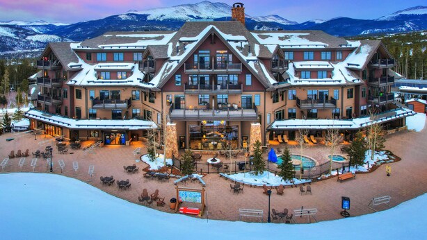 Un hotel grande de varios pisos con un patio central, asientos exteriores y vistas a montañas nevadas.