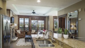 Cocina moderna con encimeras de granito, pileta de acero inoxidable y estufa integrada. Cuenta con un área de estar con sofá y mesa de centro, y un balc ón con vistas a las montañas.