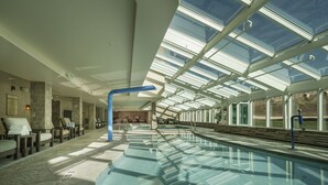 Una amplia piscina interior con techo de cristal, sillas de descanso y suelo de baldosas de piedra.
