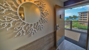 A hotel entrance with a decorative wall, a round mirror, and a view of a building and palm trees.
