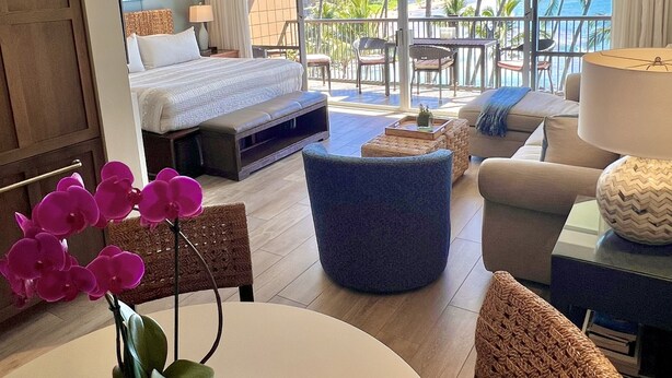 A hotel room with a balcony, a bed, a seating area, and a view of the ocean.