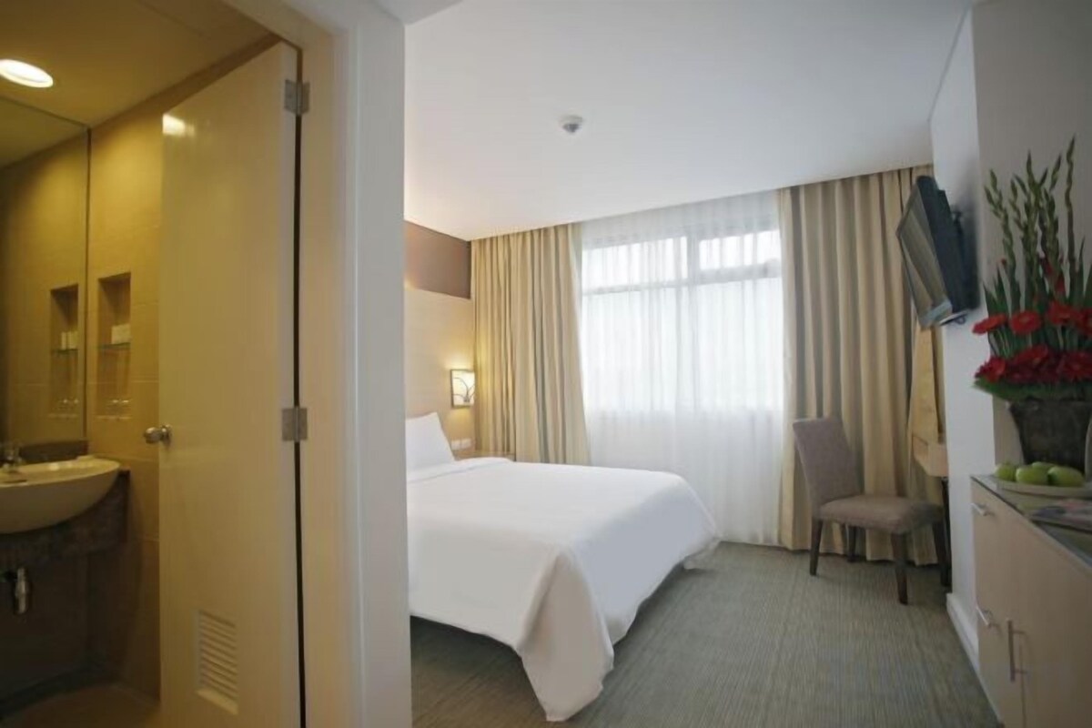 Une chambre d’hôtel avec un lit, une chaise, un bureau, un lavabo et un miroir.