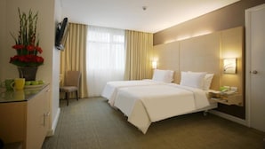 A hotel room with a large bed, a desk with a vase of flowers, a chair, and a bedside table with a lamp.