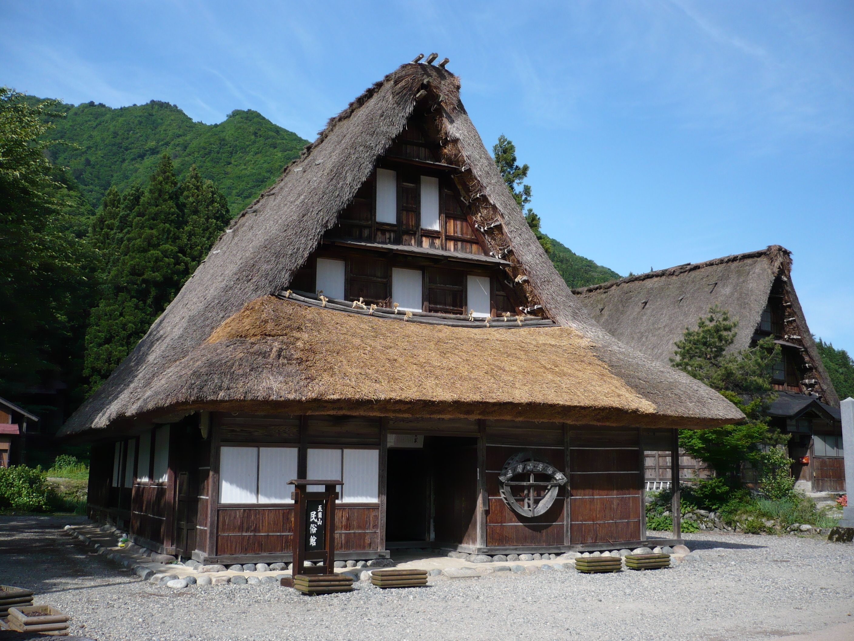 A traditional wooden building with a thatched roof, a wooden entrance, and a stone pathway leading to it.