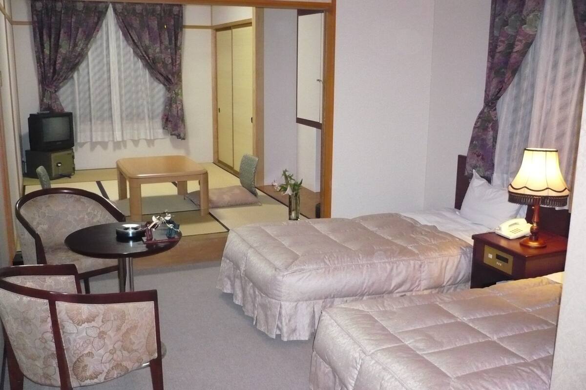 Habitación de hotel con dos camas, un escritorio, una silla, un televisor y una lámpara.