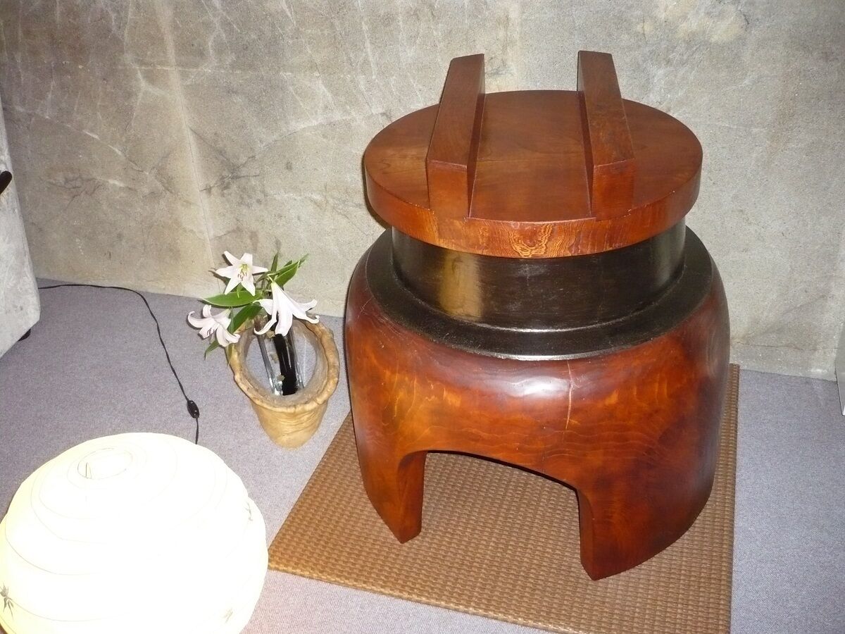 A wooden stool with a circular top and a flat base, placed on a textured mat.
