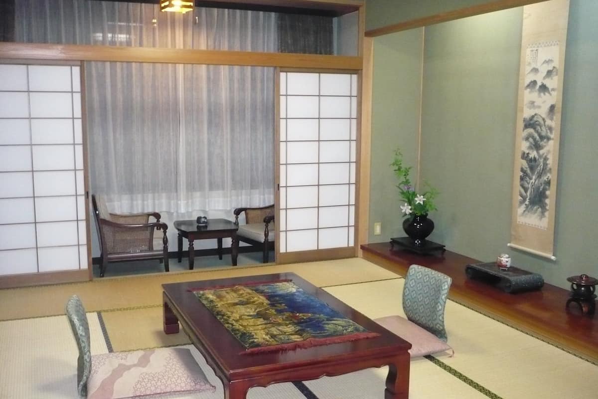 Una habitación tradicional japonesa con suelo de tatami, una mesa de madera baja con un colorido tapete, un sofá y un puertas correderas shoji.
