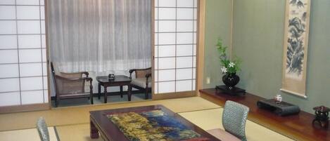 A traditional Japanese room with tatami flooring, a low wooden table with a colorful mat, a sofa, and a sliding shoji screen door.