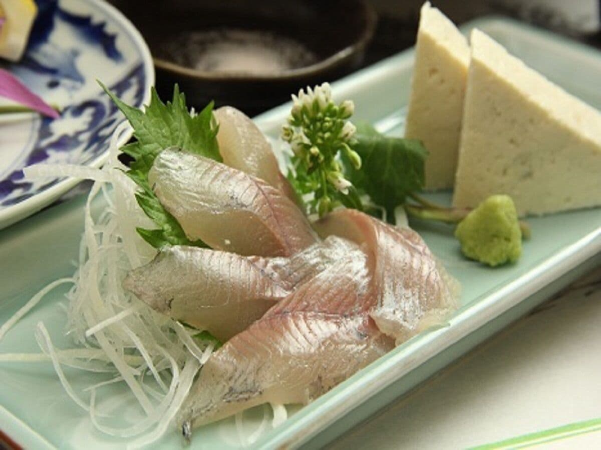 Een bord sashimi met dun gesneden vis, versierd met groene bladeren en een klein beetje wasabi.