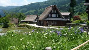 Traditional thatched-roof houses with a river in the foreground and a mountainous backdrop. - Akao-Kan (Nanto)