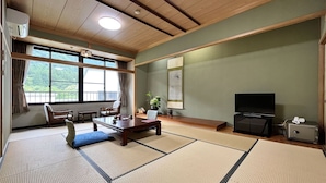 A traditional Japanese-style living room with tatami flooring, a low wooden ceiling, and a large window offering a view of greenery. - Akao-Kan (Nanto)