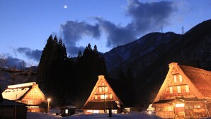 A row of wooden cabins with thatched roofs, surrounded by snow-covered ground and mountains in the background. - Akao-Kan (Nanto)