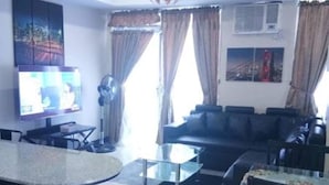 Ein modernes Wohnzimmer mit Essbereich, ausgestattet mit einer Couch, einem Couchtisch, einem Fernseher und einer Pendelleuchte.