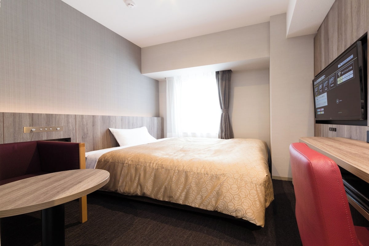 A modern hotel room with a bed, a desk, a chair, and a TV.