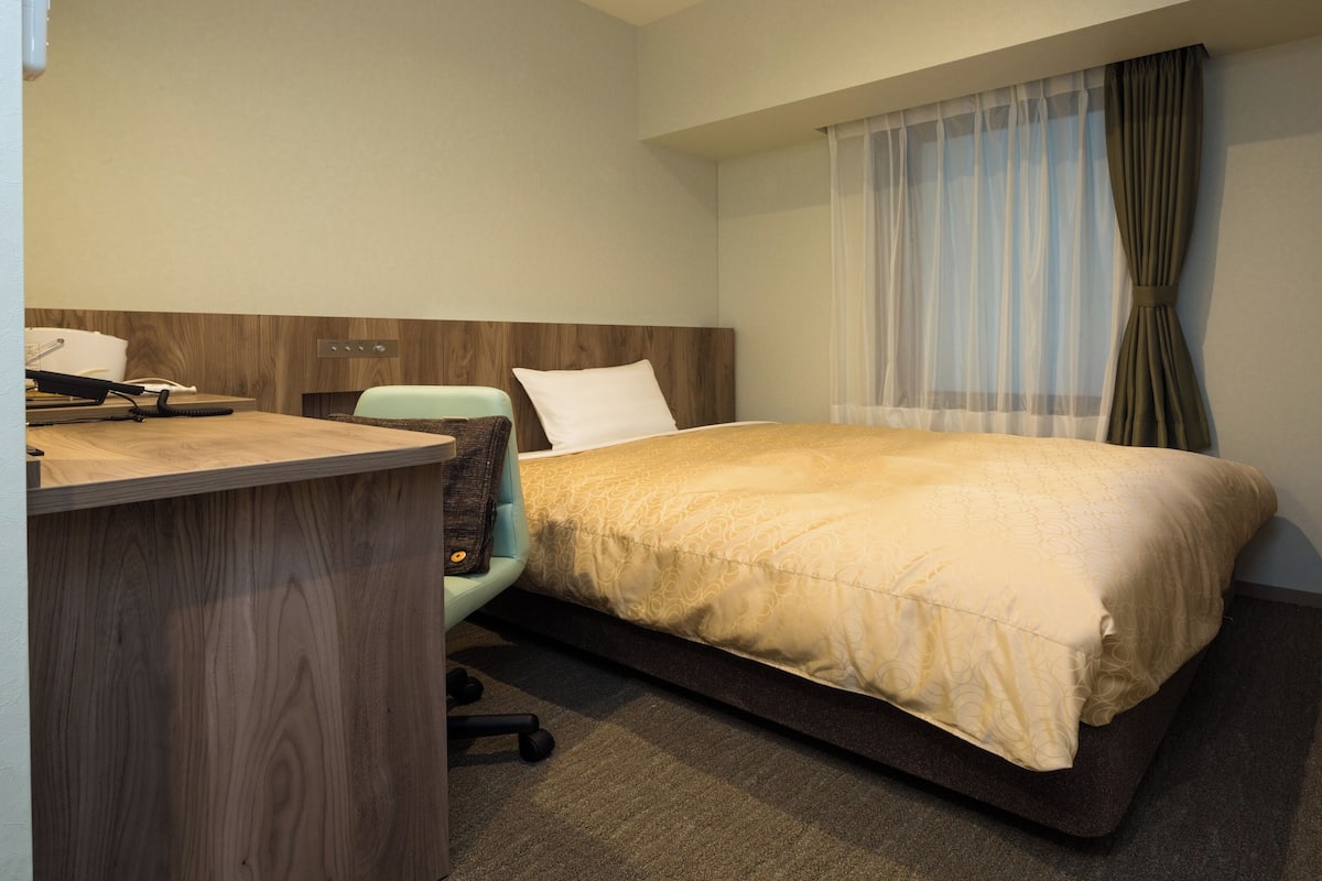 A hotel room with a bed, desk, chair, and a television.