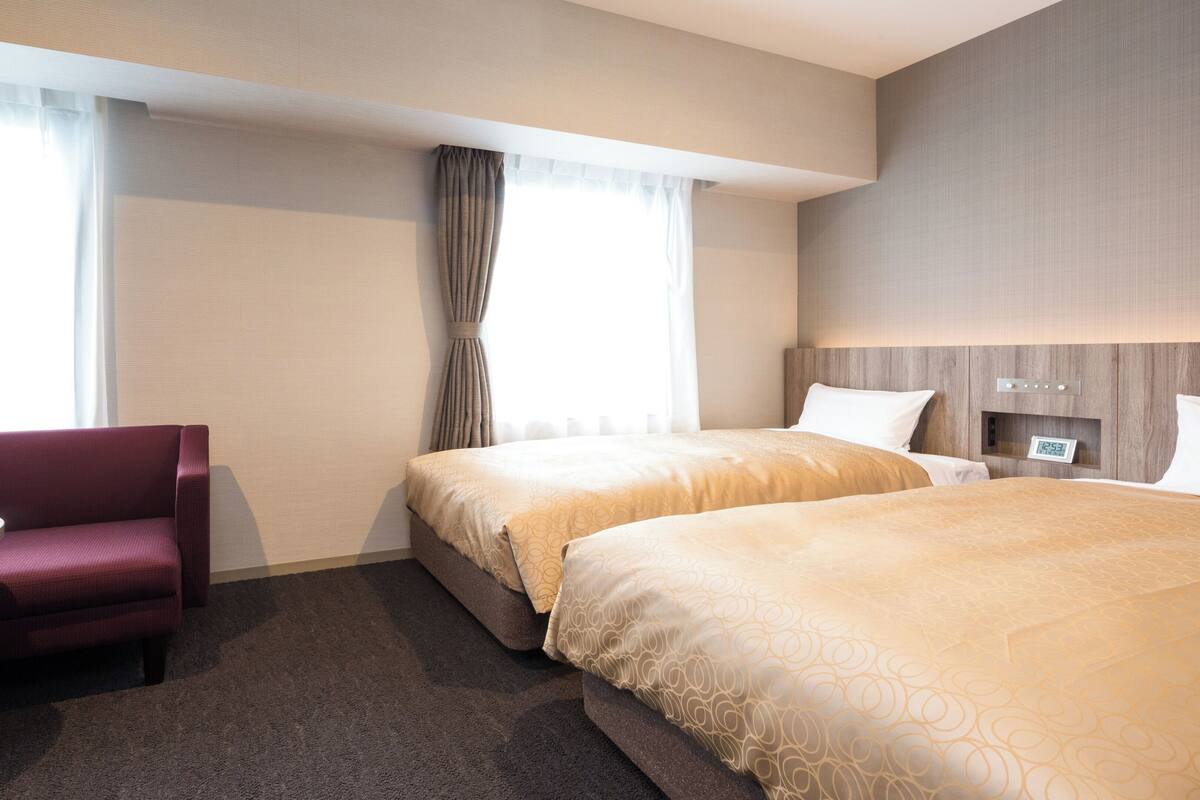 Une chambre d’hôtel avec deux lits, une petite table, un canapé et une fenêtre avec des rideaux.