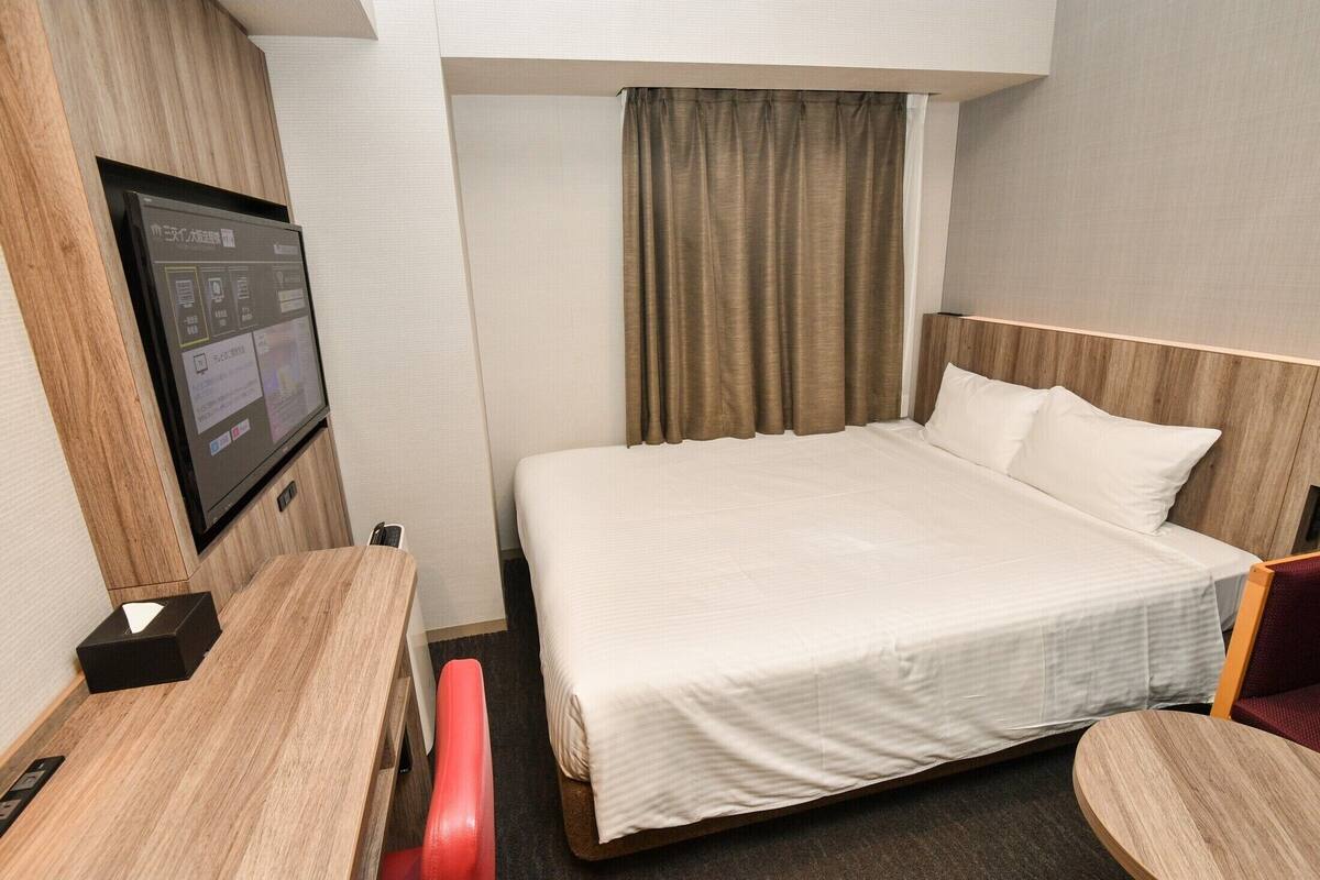 Une chambre d’hôtel équipée d’un lit, d’un bureau, d’une chaise et d’un téléviseur fixé au mur.
