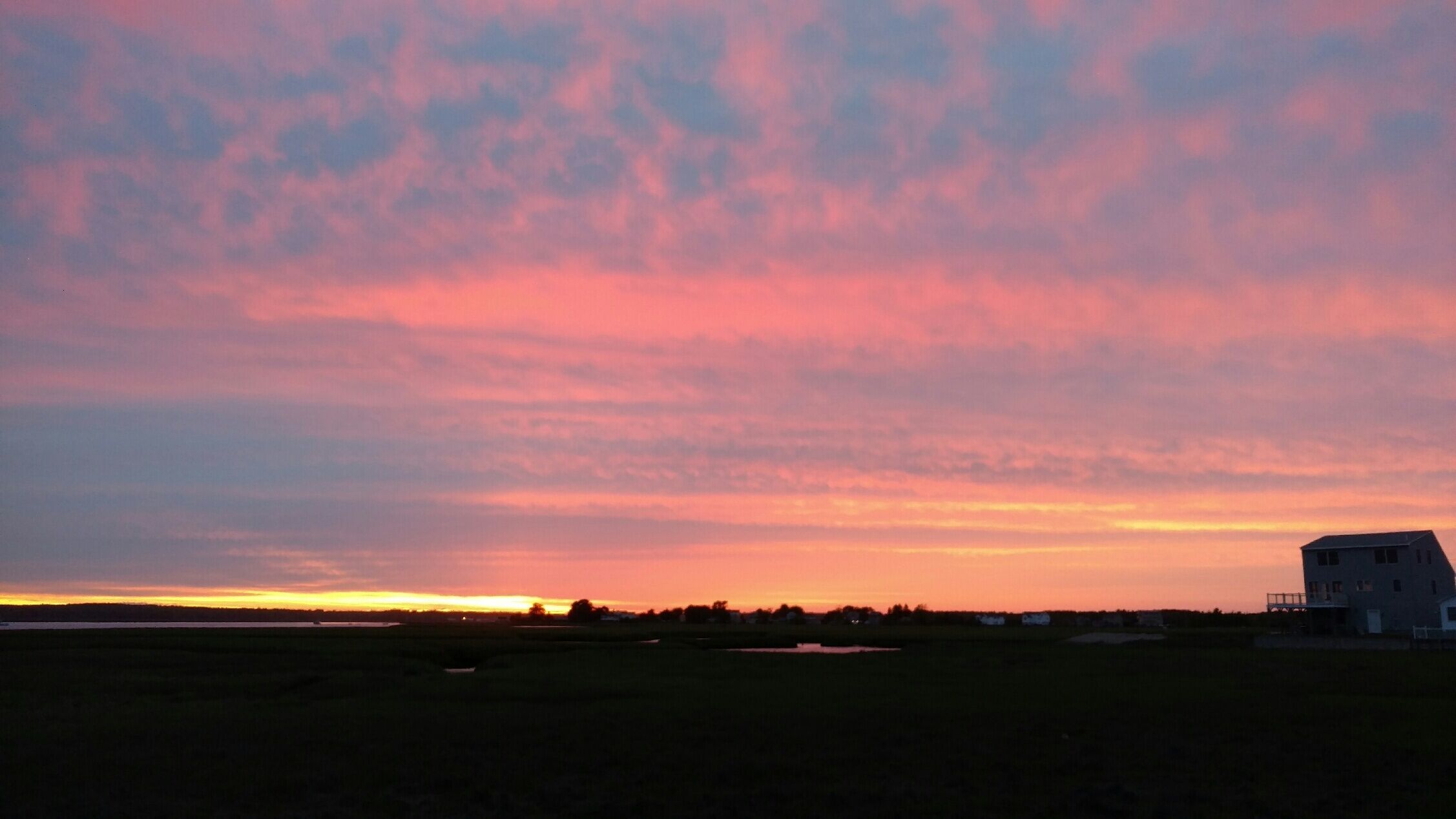 A rural landscape with a house at sunset.