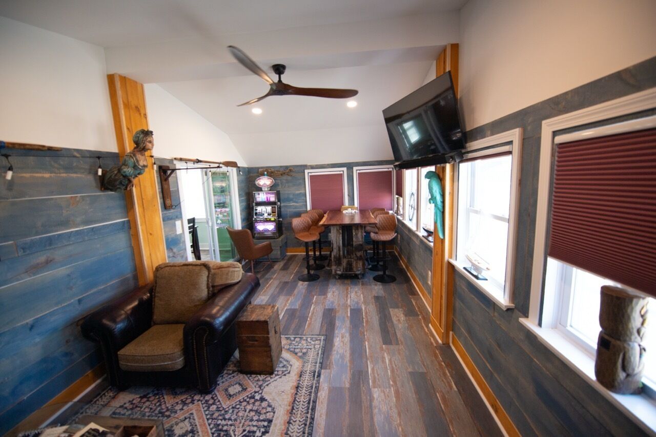 A cozy room with a wooden floor, a leather sofa, a dining table with chairs, a ceiling fan, and a television mounted on the wall.