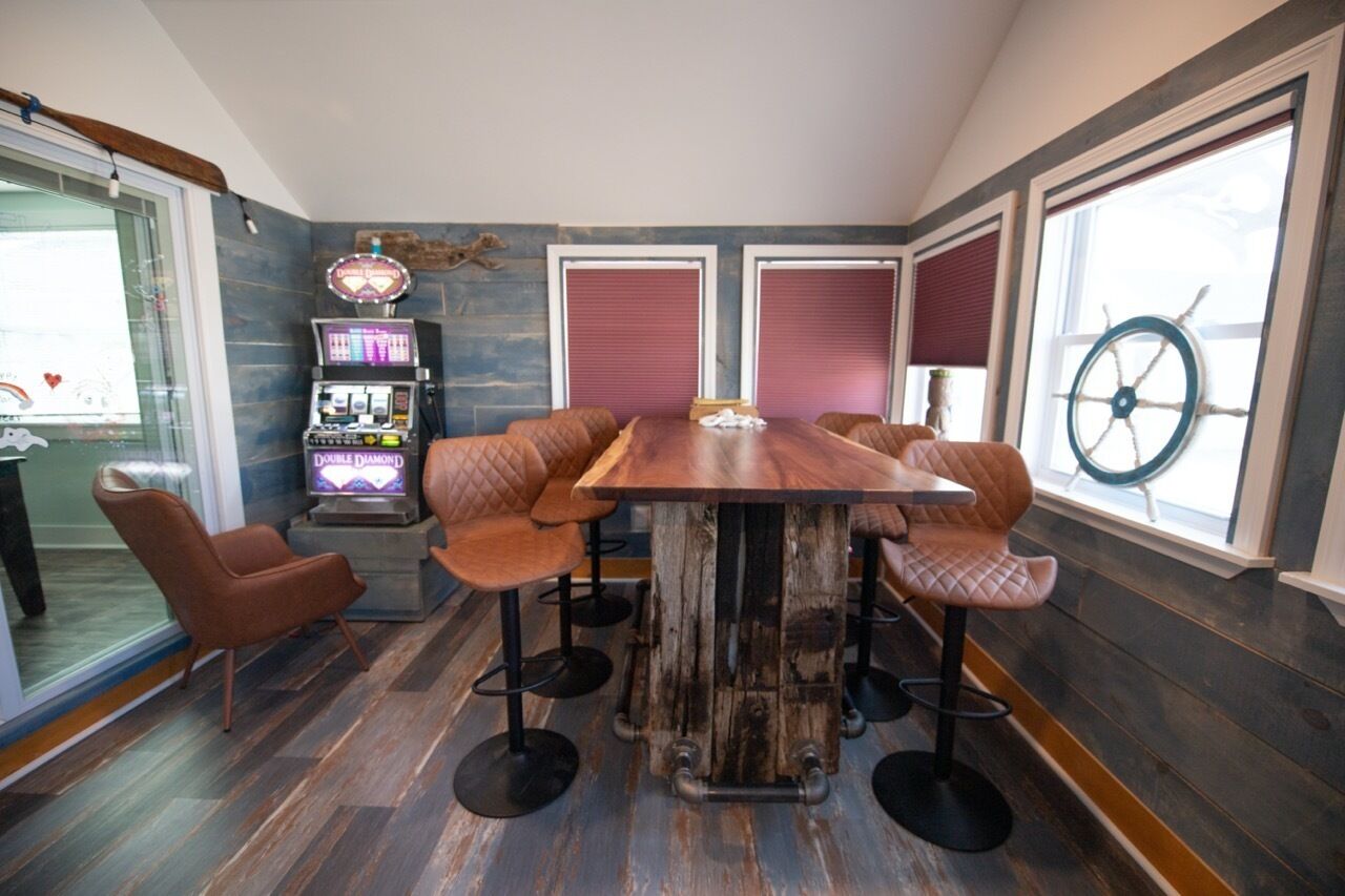 Un comedor con una mesa de madera y sillas acolchadas, un radiolas y ventanas grandes con contraventanas.