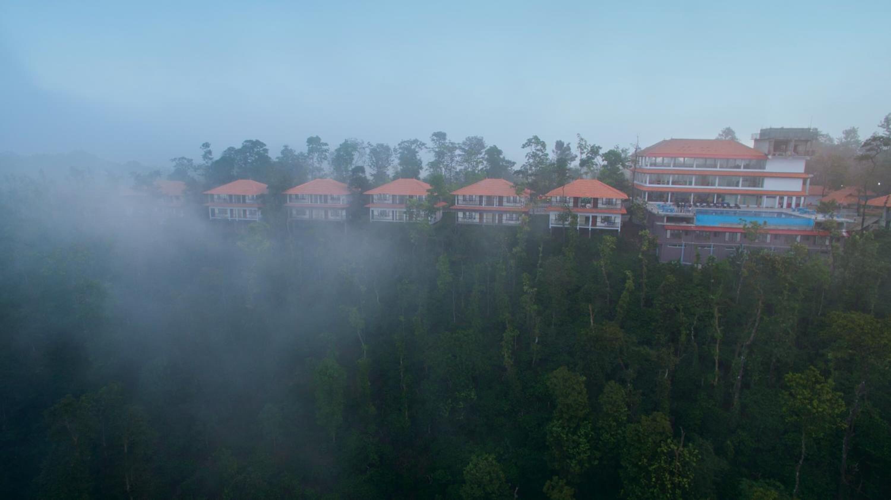 A row of red-roofed buildings with multiple floors, surrounded by dense forest.