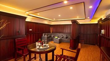 A spacious living area with a round dining table, red chairs, a grey sofa, and wooden paneling.