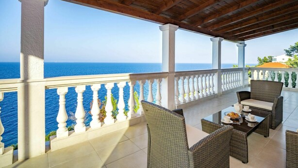 Un espace extérieur abrité, aménagé avec des meubles en osier et une balustrade blanche, offrant une vue sur la mer.