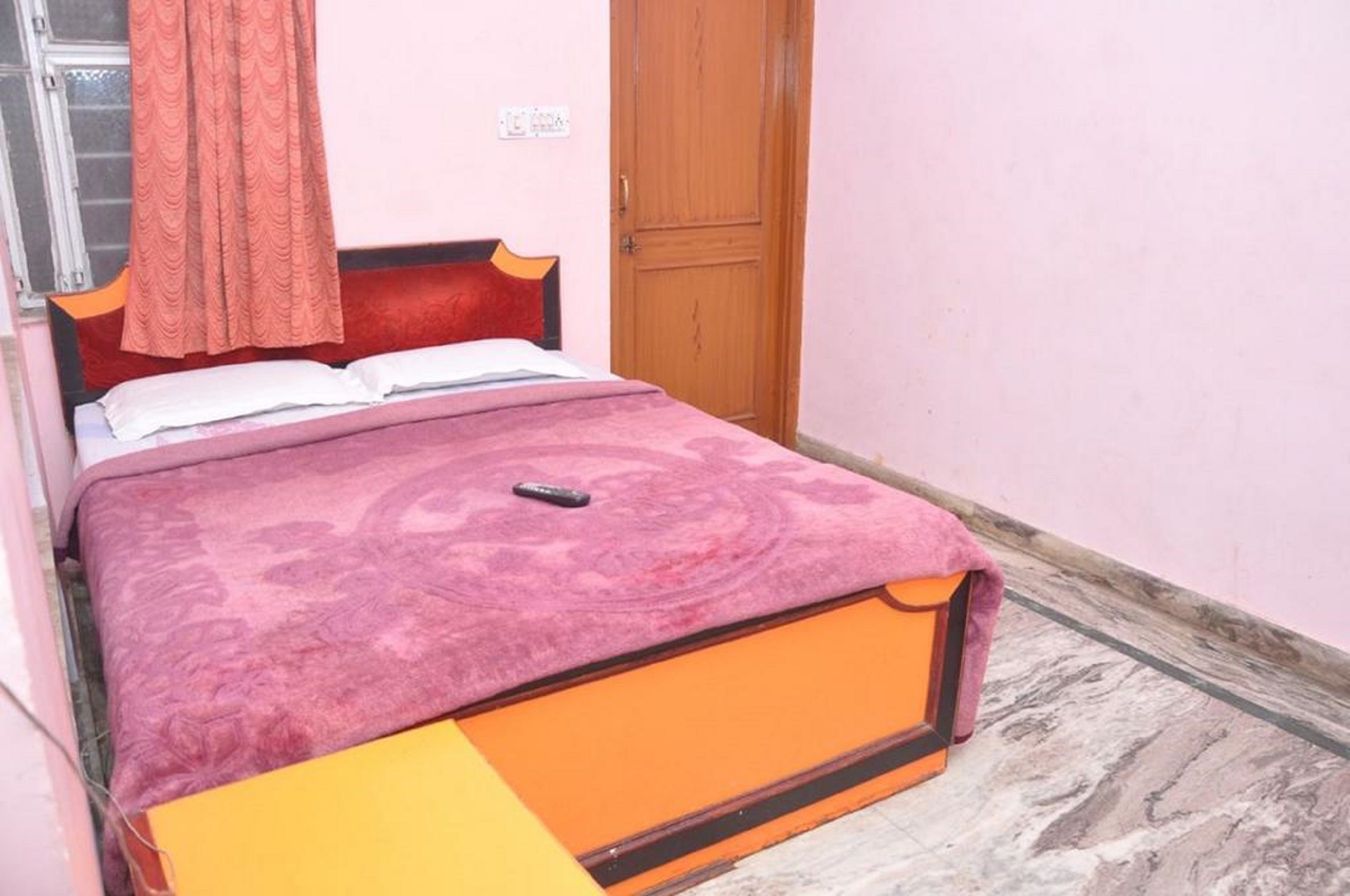 A single bed with a patterned bedspread, a wooden headboard, and a wooden door in a room with pink walls.