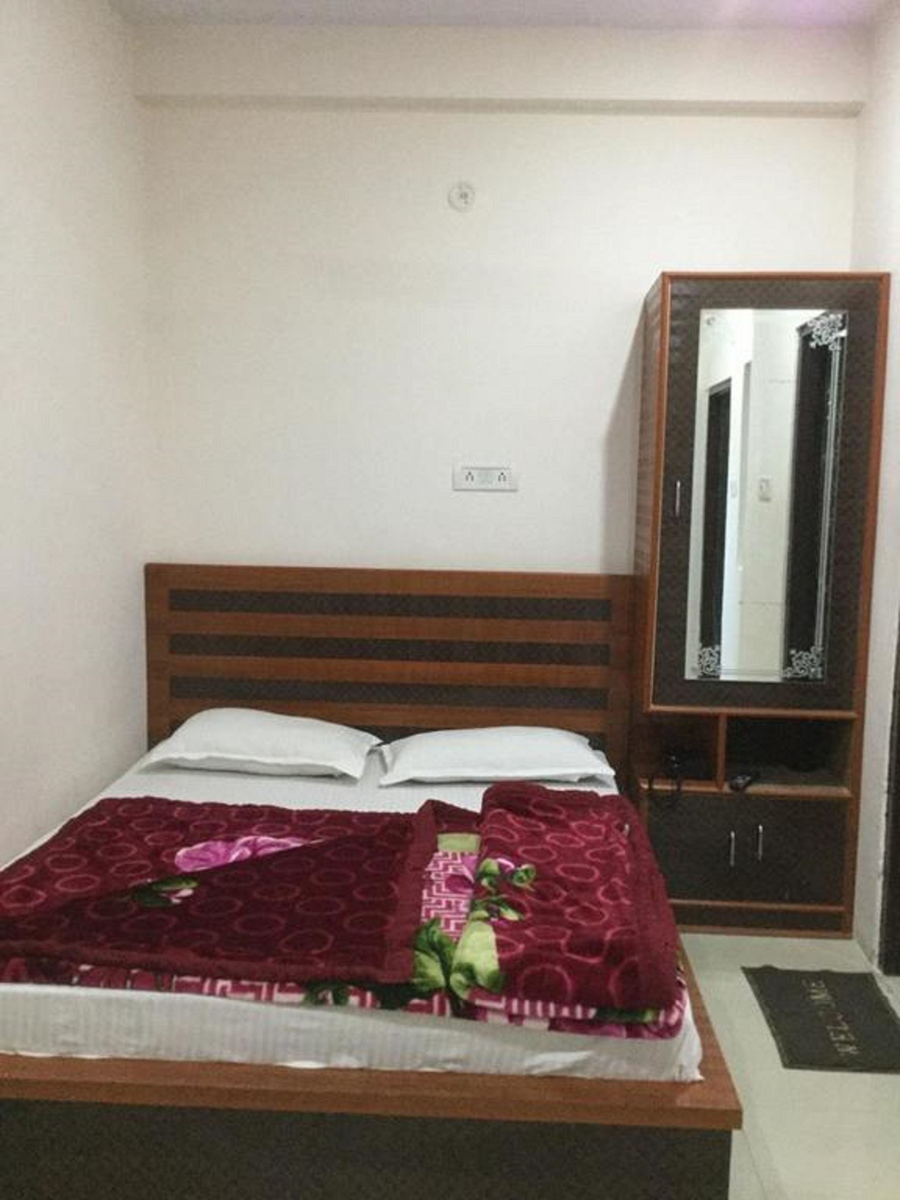 A neatly made bed with a dark red blanket and pillows, a wooden headboard, and a small wooden cabinet with a mirror.