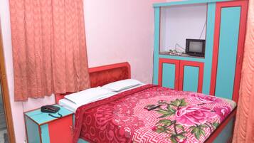 A bedroom with a bed, a wardrobe, a small table with a telephone, and a television on top of the wardrobe.