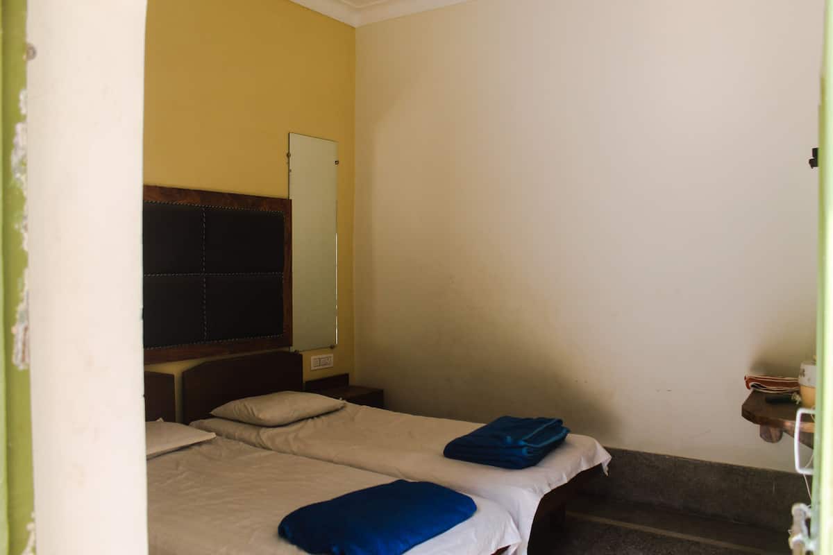 Um quarto pequeno e simples, com duas camas, um espelho e uma mesinha.