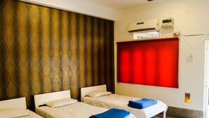 Una habitación de hotel con dos camas individuales, una cortina roja, un equipo de aire acondicionado y un ventanal pequeño.