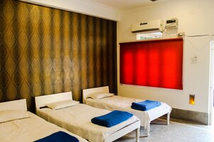 A hotel room with two single beds, a red curtain, an air conditioning unit, and a small window.