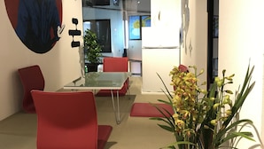 A modern interior with a glass table, red chairs, a potted plant, and artwork on the walls. - bnb+ Ninja Otsuka - Hostel (Tokyo)