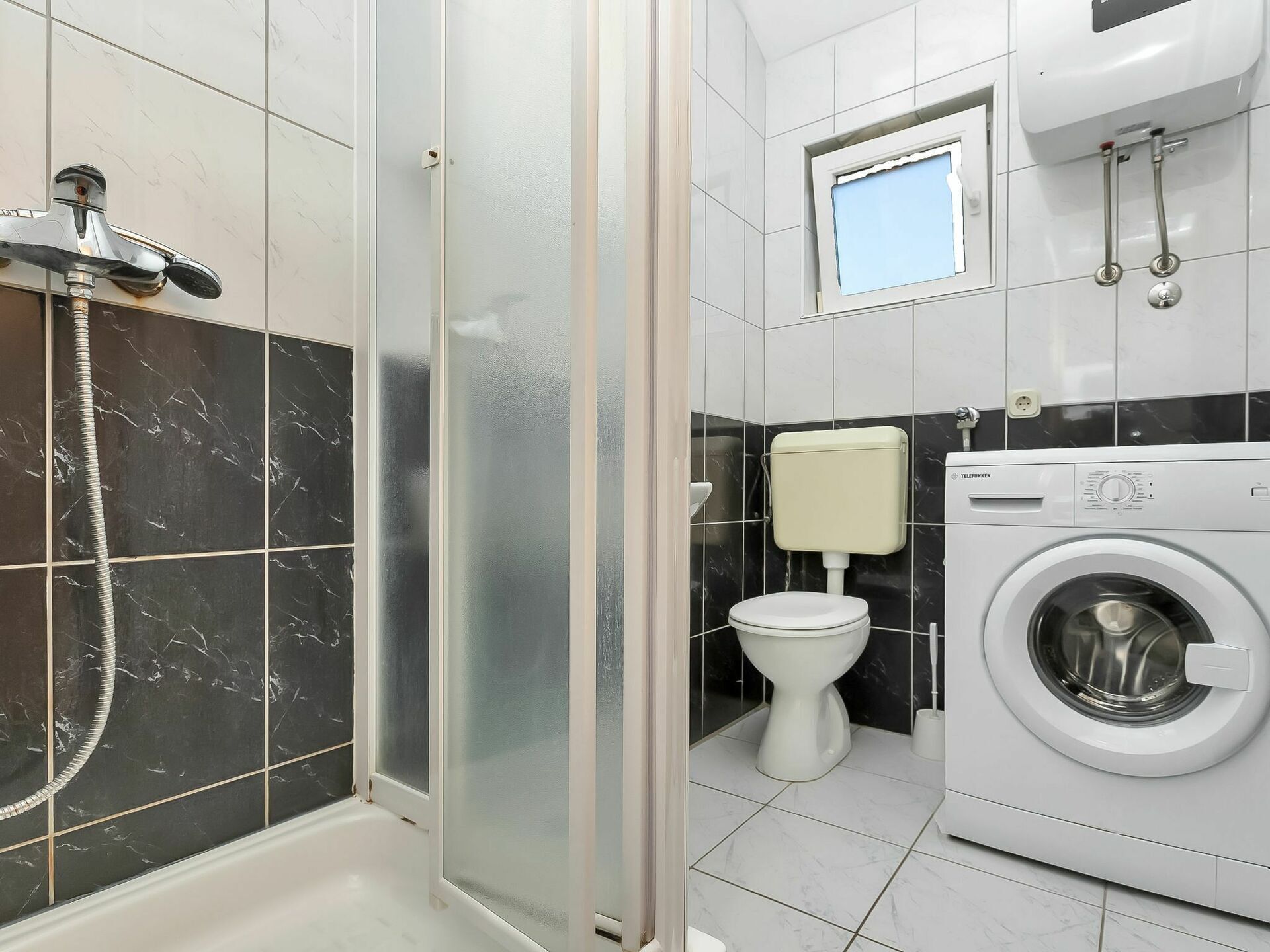 A bathroom with a shower, toilet, and washing machine.