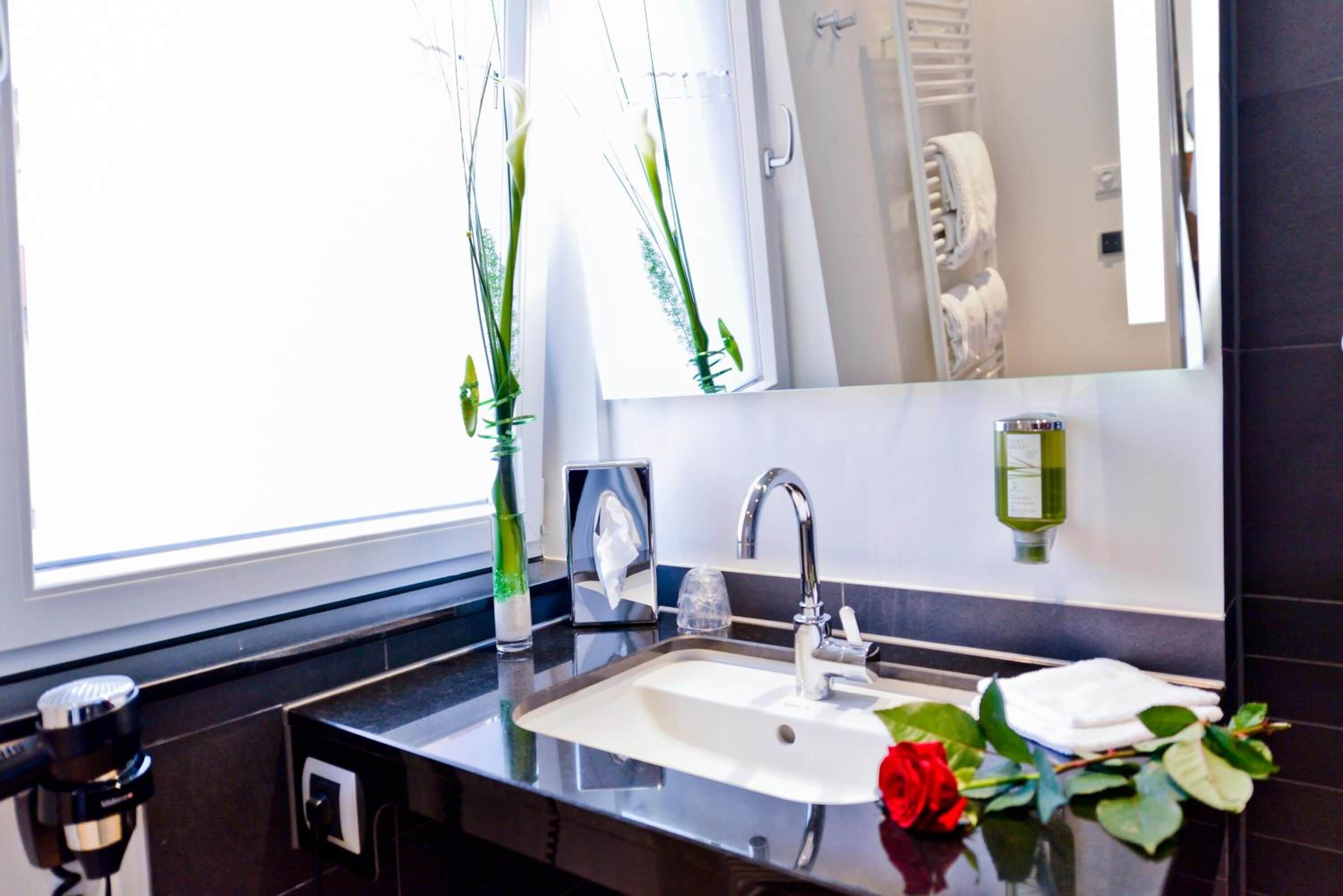 A modern bathroom with a large mirror, a sink, and a window with plants.
