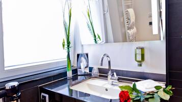 A modern bathroom with a large mirror, a sink, and a window with plants.