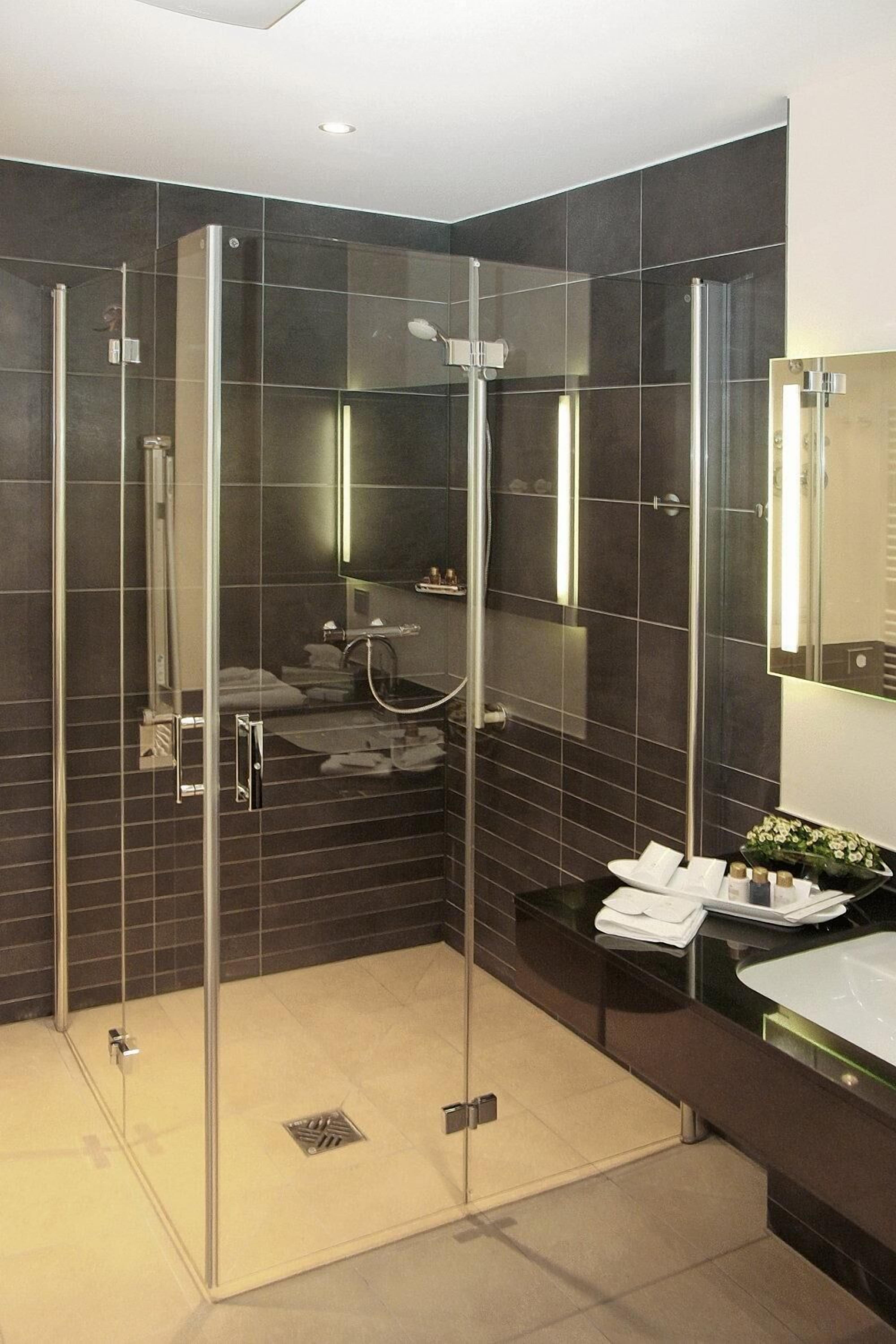 A modern bathroom with a glass-enclosed shower, dark tiled walls, and a vanity with a mirror.